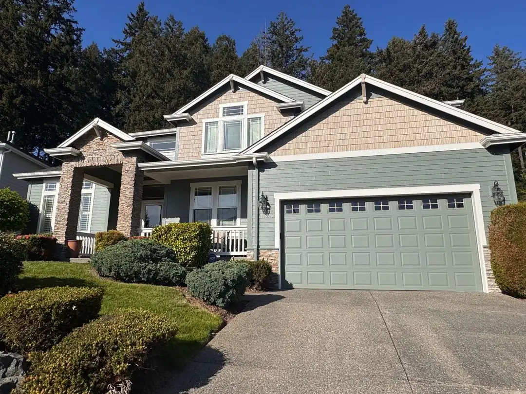 Two-story home repainted sage green with tan shingle gables by Premier Paint & Construction