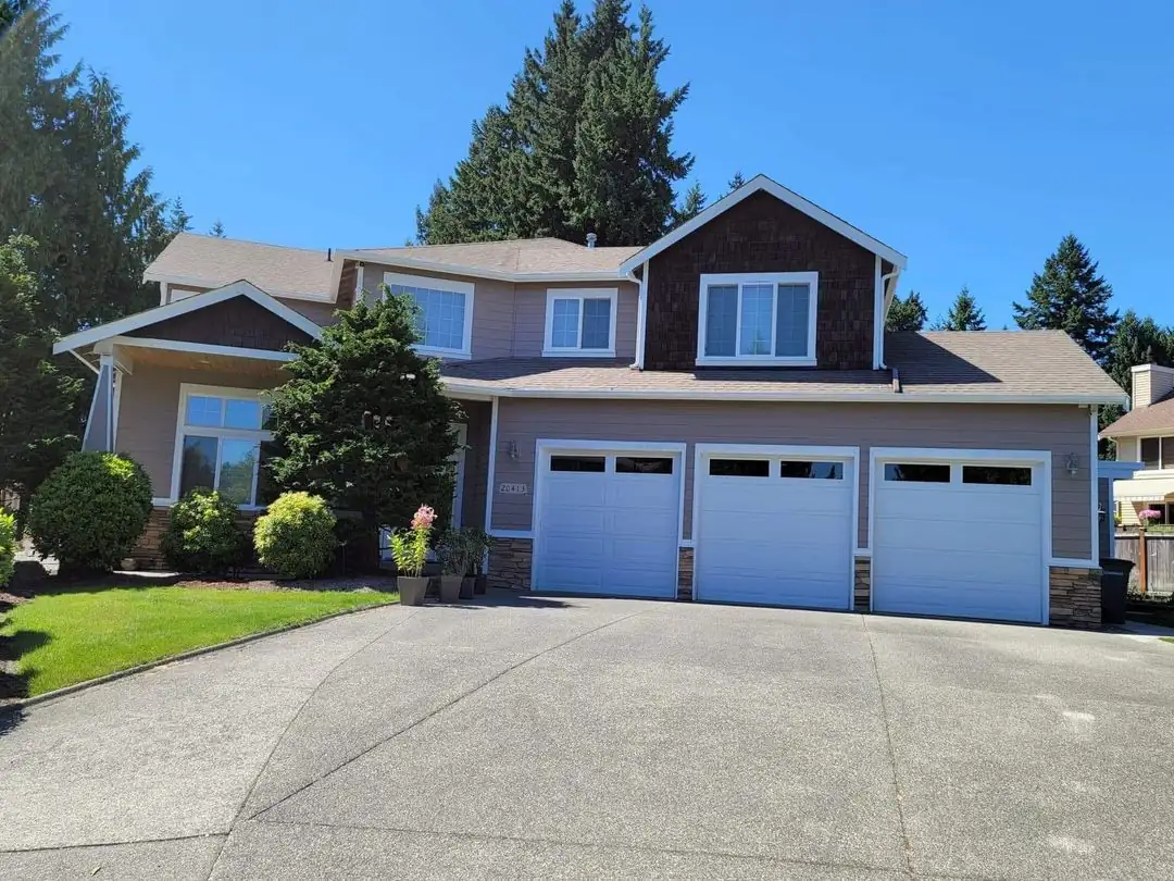 Two-story home with three white garage doors after an exterior repaint by Premier Paint & Construction